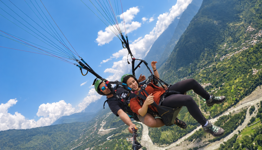Tandem paragliding pilot and passenger flying above the Kullu Valley in Dobhi